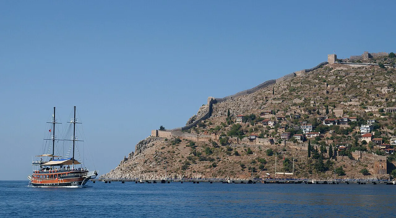 A tour boat heading towards Alanya harbour beneath the castle hill.