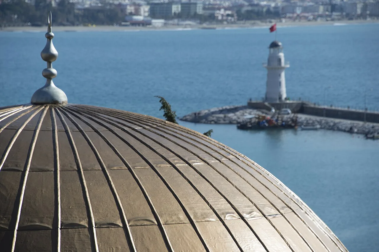 The Alanya lighthouse seen beyond a mosque dome.