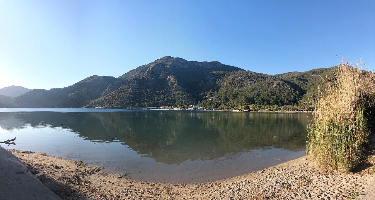 A calm cove on the Ölüdeniz shore with wooded hills beyond.