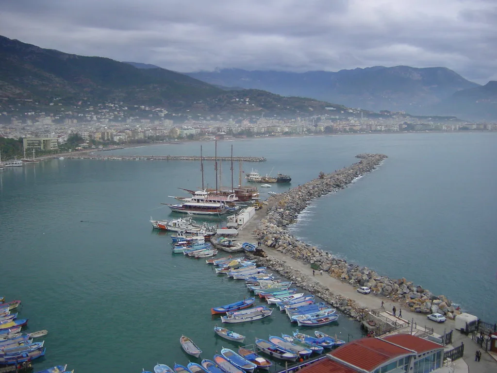 Alanya harbour and its breakwater seen from above, with mountains behind.