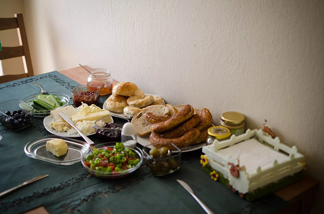 A home-style Turkish breakfast table with bread, sausages and small plates of cheese and vegetables.