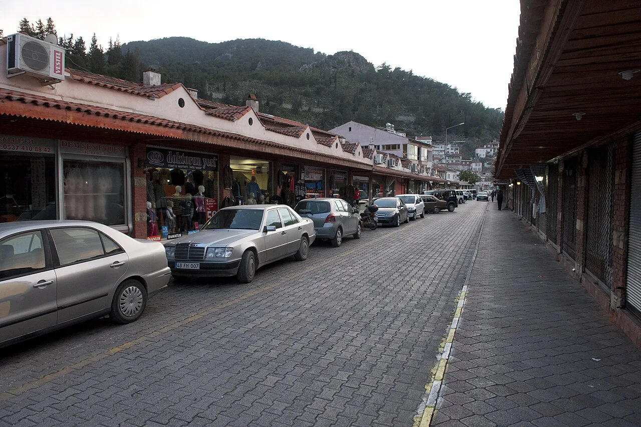 A shop-lined arcade street in Fethiye with wooded hills behind.