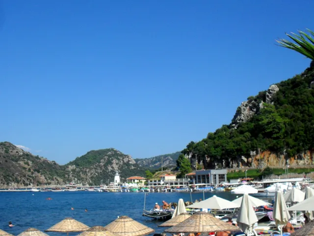 Parasols on the beach at İçmeler beneath wooded hills.
