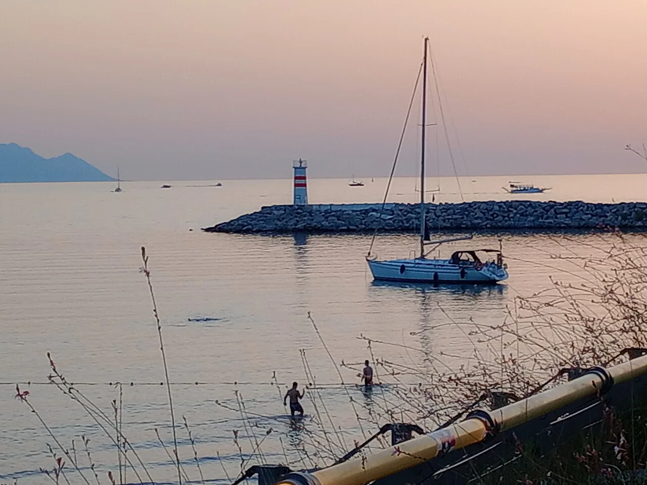 A sailing boat and the harbour lighthouse off the beach at Kuşadası.