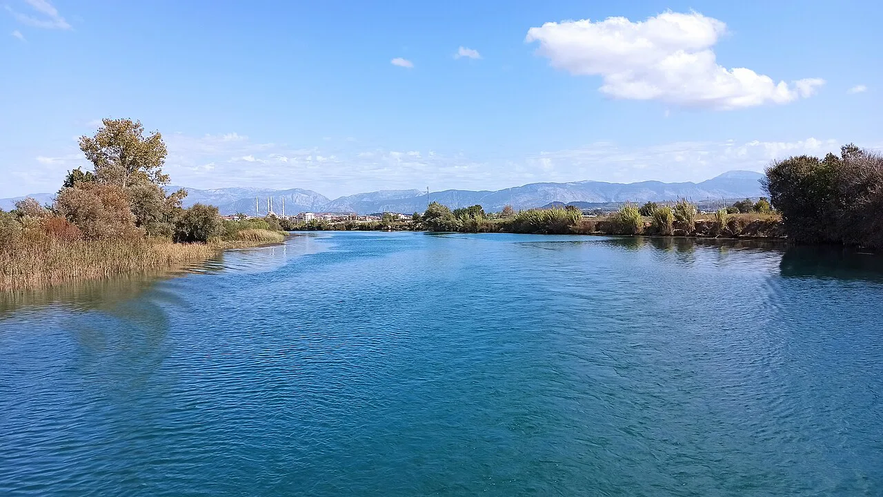 The broad blue Manavgat River lined with reeds and trees.