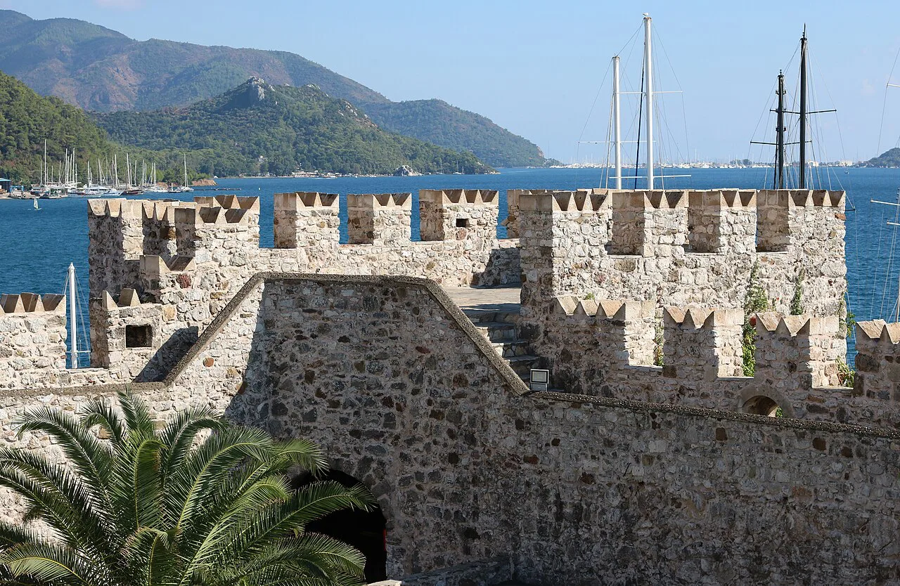 The battlements of Marmaris Castle with yacht masts in the marina beyond.
