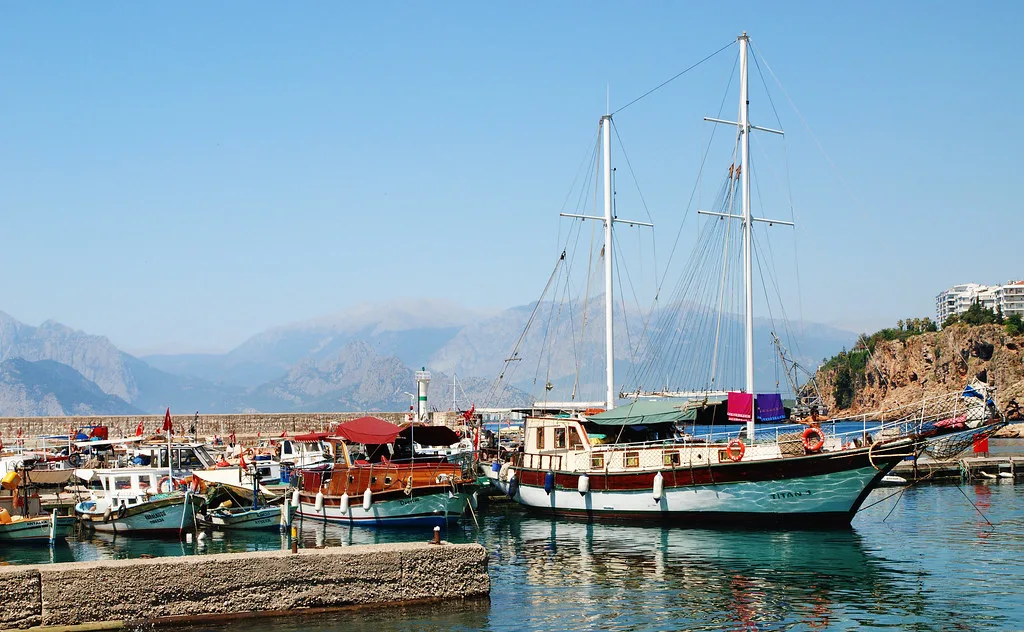 A gulet and fishing boats moored in Antalya harbour with mountains beyond.