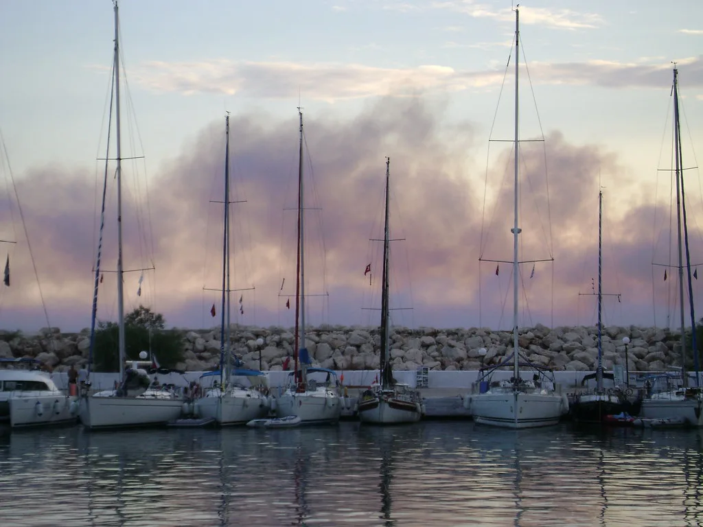 Yachts in Kalkan harbour at dusk under a haze of smoke from a forest fire.