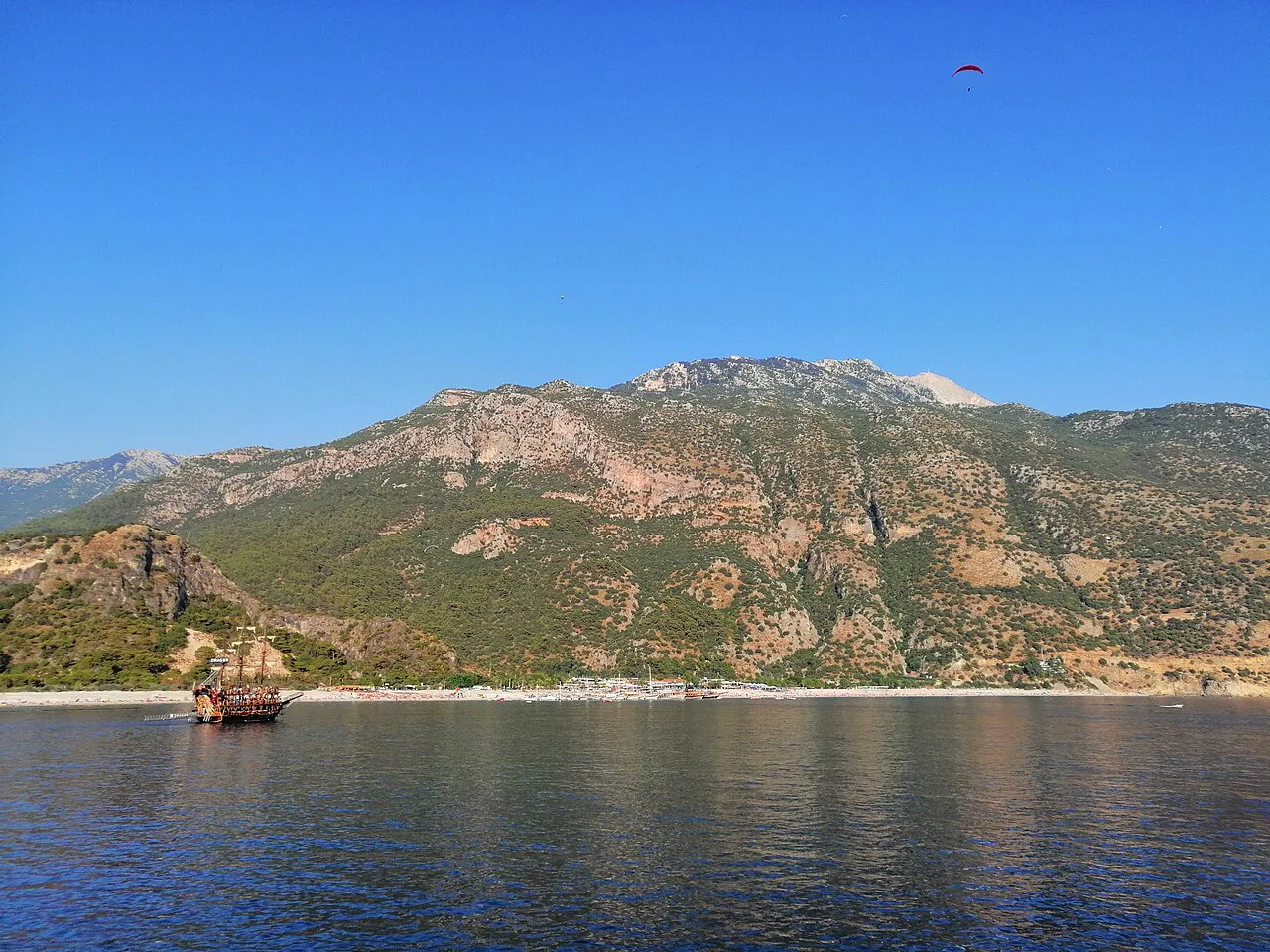 A tour boat on the water at Ölüdeniz beneath the mountains.