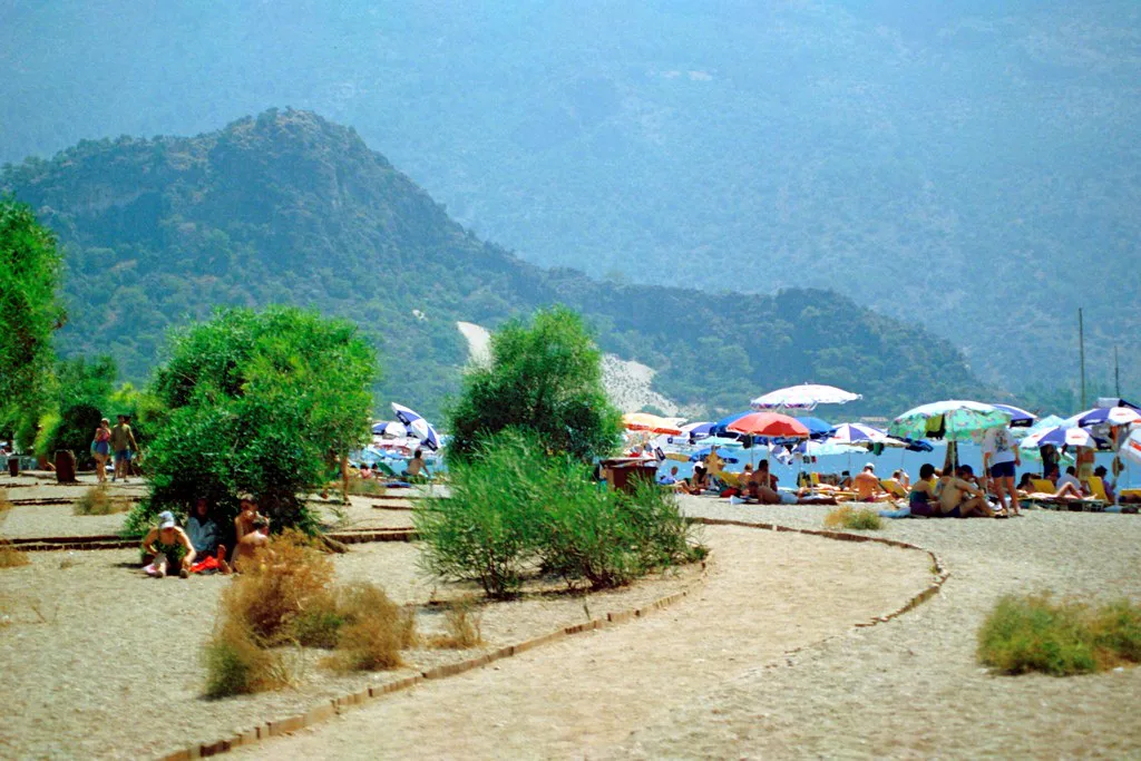 Sunshades on the beach at Ölüdeniz beneath wooded mountains.