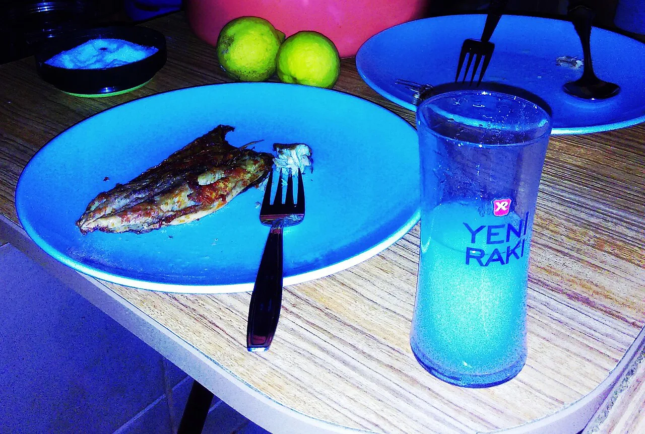 A glass of Yeni Rakı beside a plate of grilled fish.