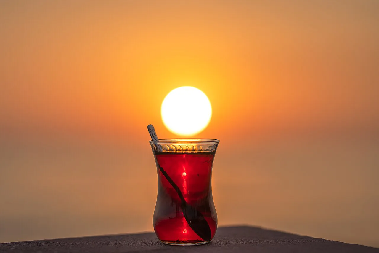 A glass of Turkish tea held up against a sunset.